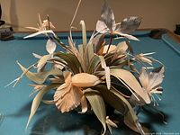 Image showing artificial floral arrangement with cream and beige flowers and various leaves on a blue surface.
