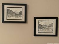 Two black and white framed prints on a beige wall, one showing Byward Market and the other the Rideau Canal.
