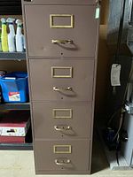 Photo showing front view of a brown metal filing cabinet with four drawers, brass-colored handles, and label holders.