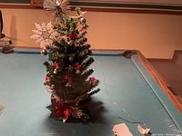 Photo of mini Christmas tree on a pool table with decorations and power adapter cable.