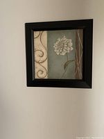 Square framed floral wall art showing a white flower with a stylized background in beige and blue-gray colors.