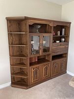 Front side view of retro wall unit showing wood grain finish, glass display cabinets, open shelves, drawer and lower storage cabinets.