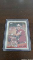 Photo of 1988 Topps Joe Montana football card in protective plastic sleeve on a dark surface.