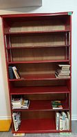 Front view of red wooden book shelf containing books on some shelves showing the overall structure and condition with visible scratches.