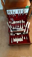 Photo showing the entire wooden canteen with the pullout drawer open, containing the silverplate flatware for eight and serving utensils arranged inside a velvet lining.