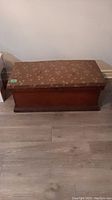 Front angle view of small cedar chest showing rectangular wooden base and vinyl top with floral pattern and visible wear.