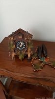 Wooden cuckoo clock on a wooden table with pine cone weights and decorative bird and leaf element placed beside it.