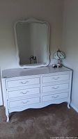 Front view of white dresser with six drawers and attached mirror, table lamp on top