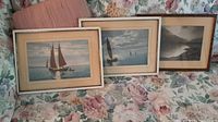 Three framed pictures laid out on floral fabric; two sailboat scenes and one landscape