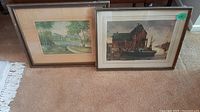 Two framed pictures side by side, showing their general size and condition on carpeted floor.
