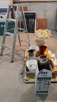 Full view of four foot aluminum step ladder with potting and gardening items arrayed on yellow cloth.