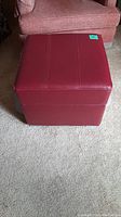 Front view of red leather square storage ottoman placed on carpet