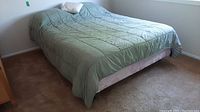 Photo of bed made with mattress, boxspring, and linens including sage green comforter and pillows.