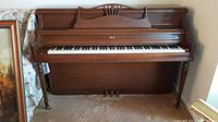 Front view of wooden upright piano with keyboard and pedals.