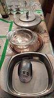 Photo showing three stainless steel serving dishes stacked and arranged with Pyrex glass pie plate and casserole dishes on a table covered with patterned tablecloth.