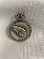 Closed silver-tone pocket watch with embossed fish design on cover.