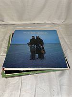 Stack of vinyl records with 'Seals & Crofts Greatest Hits' album cover on top, showing a blue beach setting with two men holding instruments.