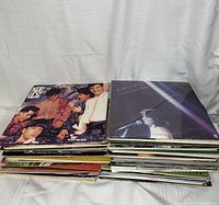 Two stacks of vinyl records showing album covers of New Kids on the Block - Step by Step and Joan Baez - From Every Stage on top, surrounded by other records to indicate quantity and variety.