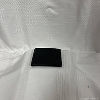 Closed surface view of black wallet on white textured fabric background.