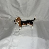 Front side view of the ceramic dachshund figure showing brown head and ears, black back, and white legs with a raised tail.