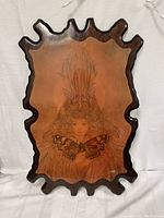 Front view of wooden art piece showing detailed image of young girl with butterfly, and ornate carved edges in dark wood finish.