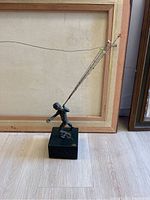 Front and side view of bronze sculpture of boy holding wires for glass balloons, mounted on black base.