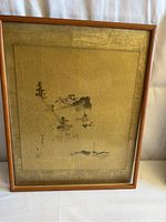 Front view of the framed watercolor painting depicting a traditional Chinoiserie landscape with mountain, trees, village, and boat, signed and stamped by the artist. Frame is wooden and shows some looseness.