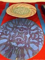 Photo showing two collectible plates, one with a blue and purple speckled abstract pattern and the other with a pink swirl pattern and green floral lattice center.