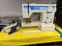 View of the sewing machine with foot pedal placed beside it on yellow table.