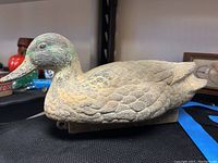 Side view of a hand-carved mallard duck decoy showing detailed feather texture and faded green paint on the head and brownish body with signs of wear.