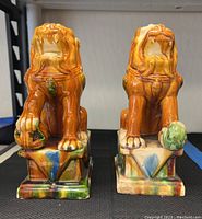 Pair of ceramic Foo dog statues placed side by side on a black surface showing front and side views, highlighting glazed multicolor finish and detailed features.