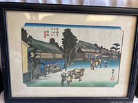 Full view of the framed woodblock print showing a street scene with figures and buildings under a blue sky gradient.