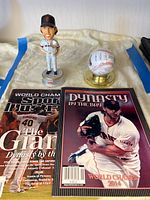 Photo showing the bobblehead figure, signed baseball in display case, and two magazines laid out on display