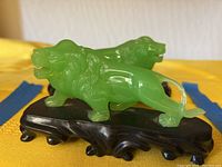 Front side view of two green resin lion figures mounted on black stands showing detailed faces and bodies