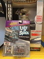 Photo showing two Lost in Space collectible toys including Robot B9 in rectangular box with Try Me sticker and a Johnny Lightning die-cast Lost in Space vehicle in blister pack attached to card.