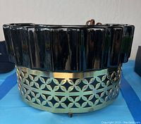 Front view of lamp showing black ceramic top with ridged design and brass base with cutout floral pattern.