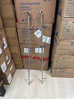 Pair of long stainless steel meat tree hooks standing upright against stacked boxes, showing length and top hanging loop.