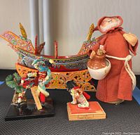 Full view of the lot showing the hand painted wooden model boat, cloth doll, and three small figurines on display.