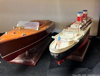 Both model boats placed side by side on a dark surface, showing wood motorboat and ocean liner front views.