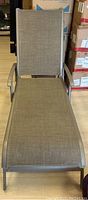 Full view of the reclining patio lounge chair showing overall seating and backrest area with light brown mesh fabric and silver metal armrests and frame.