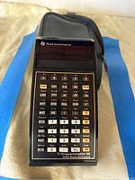 Front view of the Texas Instruments calculator with keypad and display visible, resting on blue cloth.