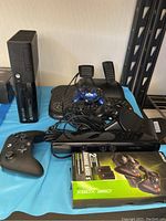 Photo of Xbox 360 console with various controllers, racing pedals, and a charging base box on a blue surface