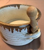 Close-up photo of small ceramic dish in white and brown drip glaze with wooden spreader in side handle.