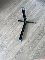 Photo of black metal indoor bike stand with extendable vertical support bar and hook and loop strap on a wooden floor.