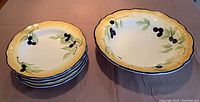 Image showing set of one large shallow serving bowl and four smaller matching bowls with yellow and white background and painted blueberries and green leaves.
