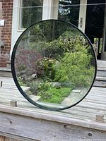 Mirror standing outside on wooden deck showing garden reflected.