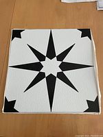 Close-up image of single floor tile with black starburst and corner accent pattern on white background.