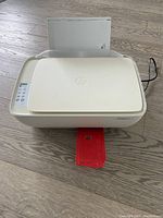 HP DeskJet 3634 all-in-one printer placed on floor with paper loaded and printed output visible.