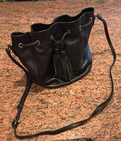 Black leather drawstring handbag with tassels and shoulder strap on marble surface