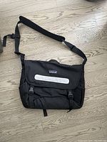 Front view of the black Patagonia briefcase showing shoulder strap, front flap with Patagonia logo, and buckle closures.